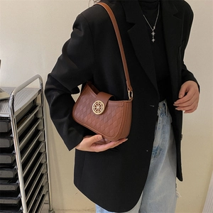Sac à bandoulière matelassé marron avec boucle dorée porté par un mannequin élégant