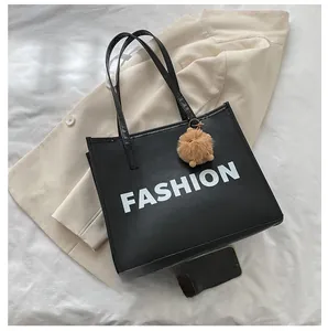 Detail of black tote bag with white FASHION lettering and a brown plush pom-pom charm