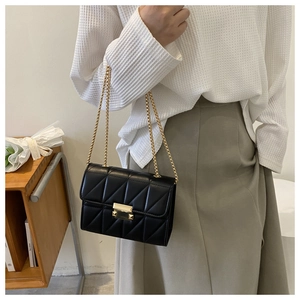 Detail of black quilted crossbody bag with gold chain strap and rectangular metal lock