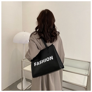 Modern black tote bag with white FASHION print styled on a shoulder in a home setting