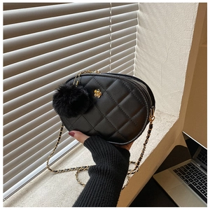 Close-up of quilted black oval bag featuring golden flower logo and fuzzy pompom charm