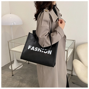 Detail of a chic black PU leather tote bag with FASHION logo print styled with a trench coat