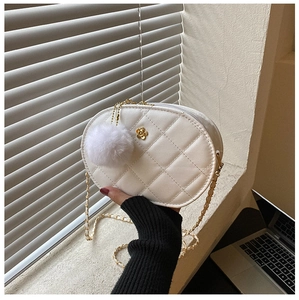 Close-up of white quilted oval crossbody bag with gold flower detail and plush pompom