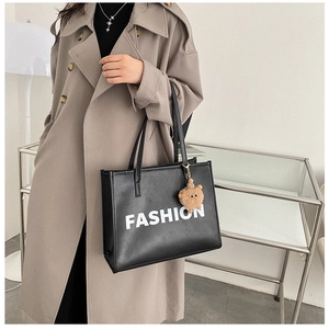 Detail of black leather tote bag with FASHION lettering and a brown plush ball charm