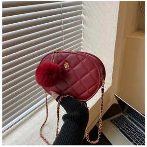 Close-up of burgundy quilted oval bag with gold flower clasp and fur ball keychain