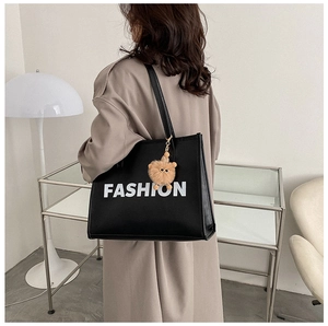 Detail of black leather tote bag featuring white FASHION print and cute bear charm