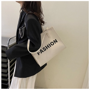 Detail of a beige tote bag with black FASHION lettering styled on a fashion model