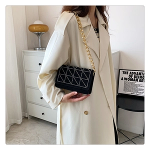 Detail shot of black velvet shoulder bag with rivet geometry and gold chain link strap