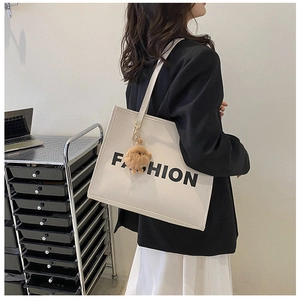 Detail of off-white tote bag featuring black FASHION text and a cute brown bear charm