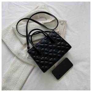 Top view of a black embossed clover handbag with shoulder strap next to a tweed jacket