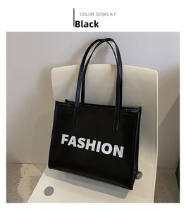 Detail of a black leather tote bag featuring a bold white FASHION print on a white chair