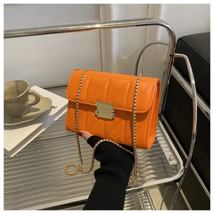 Detail of orange quilted crossbody bag featuring a gold square lock and chain strap