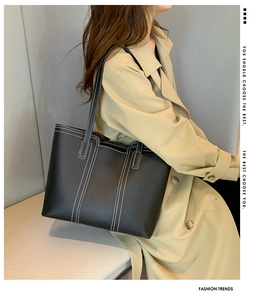 Detail of black faux leather tote with white contrast stitching on light trench coat