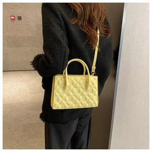 Detail of yellow crossbody bag with clover embossed pattern and gold hardware on model