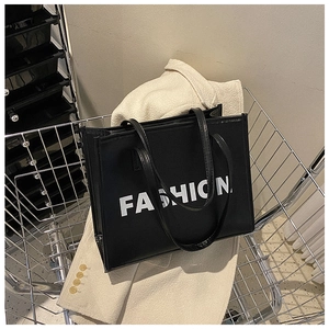 Close-up of black leather tote bag featuring bold white FASHION lettering in a shopping cart