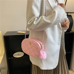 Pink quilted oval crossbody bag with gold flower detail and chain strap on white blazer