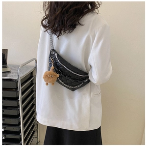 Detail of black quilted waist bag featuring dual metal chains and brown plush charm