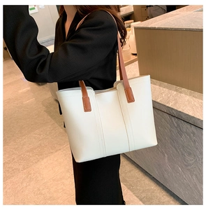 Detail view of a large cream tote bag with brown straps worn by a model in a modern room