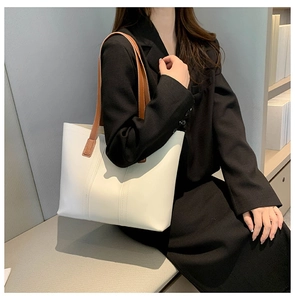 Detail view of a white leather tote bag with brown straps styled on a black blazer