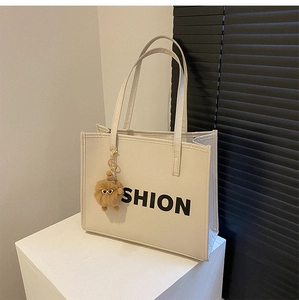 Detail of beige tote bag with black SHION text and a brown fur monster charm