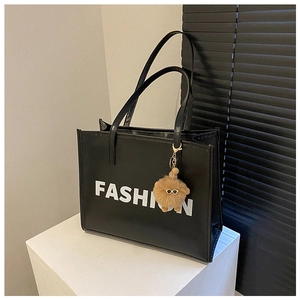 Close-up of black leather tote bag with FASHION lettering and a plush bear charm
