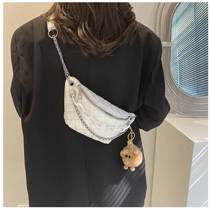 Rear view of a white quilted waist bag with chunky chain and plush charm on a black blazer