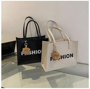Detail view of large tote bags in black and beige with fashion print and plush charms
