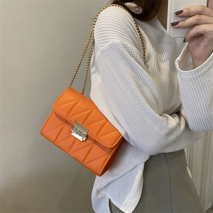 Retro orange quilted crossbody chain bag with gold buckle on a white sweater model