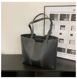 Detail of minimalist black tote bag with white contrast stitching on matte leather