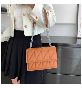 Close-up of orange quilted crossbody bag with silver chain strap on model outfit
