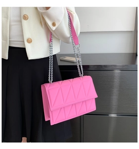 Detail of bright pink quilted crossbody bag with silver chain strap on white jacket
