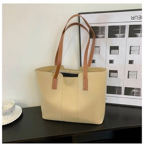 Detail view of large tote bag featuring beige body with contrast brown leather handles and stitching