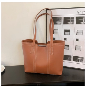 Detailed view of brown tote bag with white contrast stitching on black wood surface
