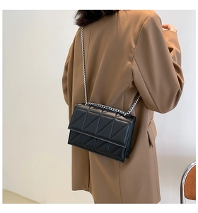 Rear view of a black quilted shoulder bag with silver chain strap on a model with a suit