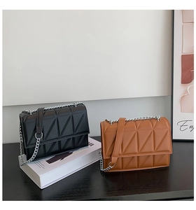 Detail view of quilted leather crossbody bags in black and caramel with silver chain straps