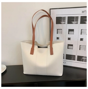 Detail view of cream tote bag with brown straps on a black surface in a home studio
