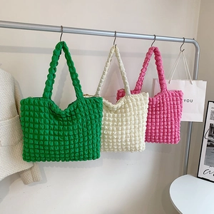 Borse tote con texture a bolle in verde, beige e rosa appese su un espositore