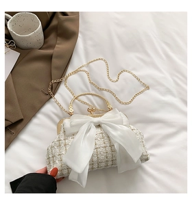 Close-up of white tweed handbag featuring a large satin bow and gold metal handle