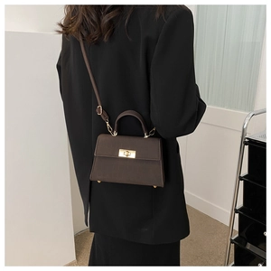 Dettaglio della piccola borsa a tracolla marrone scuro con motivo coccodrillo su blazer nero