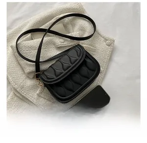 Detail of black quilted shoulder bag with gold clasp shown next to a smartphone
