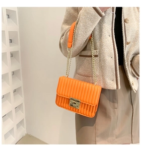 Orangefarbene strukturierte Umhängetasche mit goldener Kette am Model mit neutralem Outfit