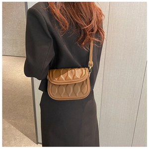 Detail of a brown textured crossbody saddle bag with gold-tone hardware on model