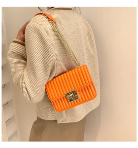 Detail einer orangen Stepptasche mit goldener Kette, getragen von einem Model