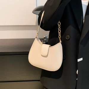 Sac bandoulière demi-lune blanc cassé chic avec chaîne dorée sur blazer noir