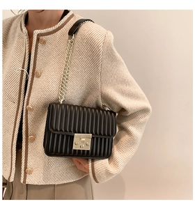 Detail der schwarzen Stepptasche mit Goldschließe an einer schicken beigen Tweedjacke