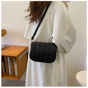 Detail of a black quilted leather shoulder bag with gold hardware on a model