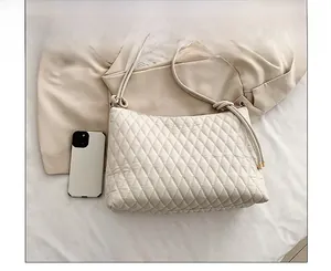 Detailed view of white quilted crossbody bag next to a smartphone for size comparison