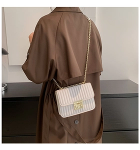 Detailansicht der beigefarbenen Plissee-Umhängetasche mit goldener Kette am Modell