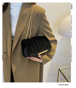 Detailed view of black velvet quilted crossbody bag with gold chain strap on shoulder