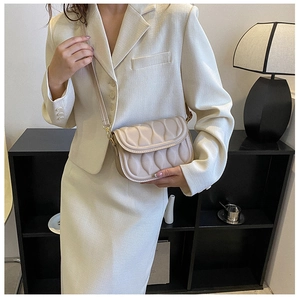 Close-up of textured cream crossbody bag with gold buckle on a white blazer